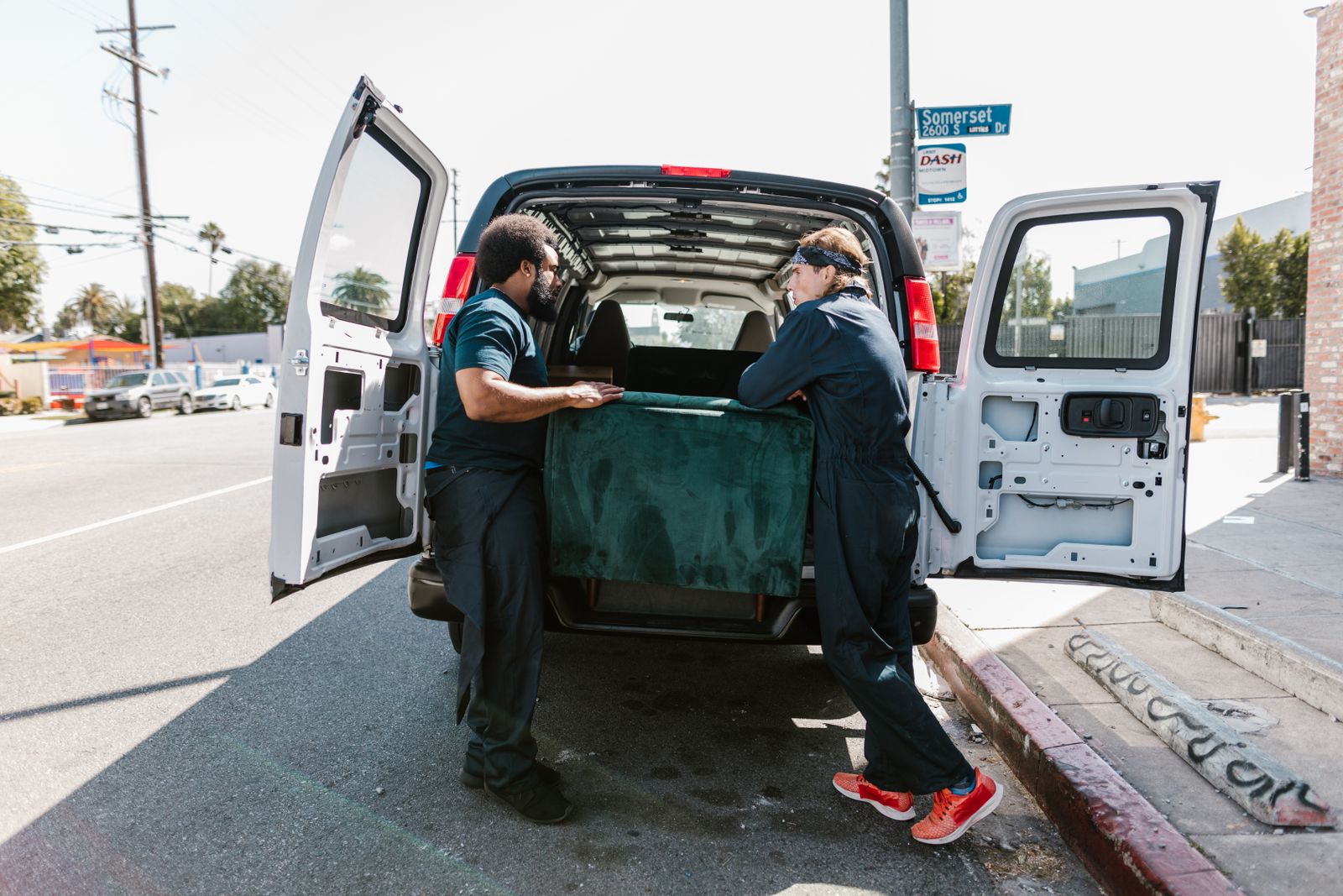 Two movers loading a green sofa into a delivery van