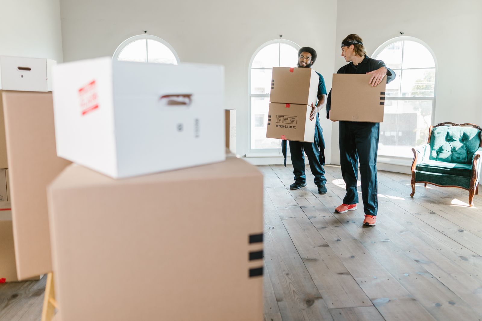 Two movers in uniform carrying boxes through an empty home